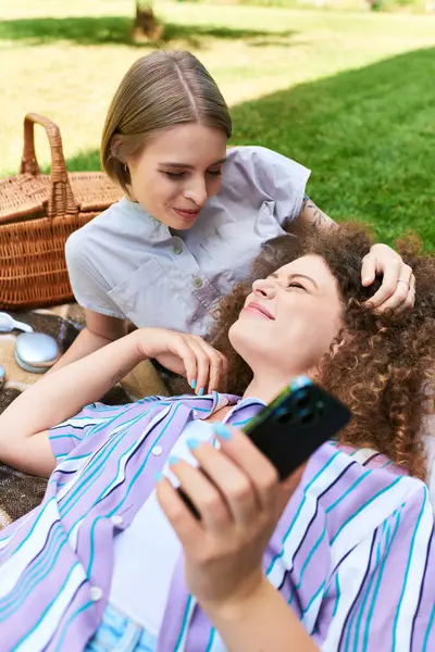 Two young women relax together on a blanket, sharing joy and warmth during a sunny day. — Stock Photo