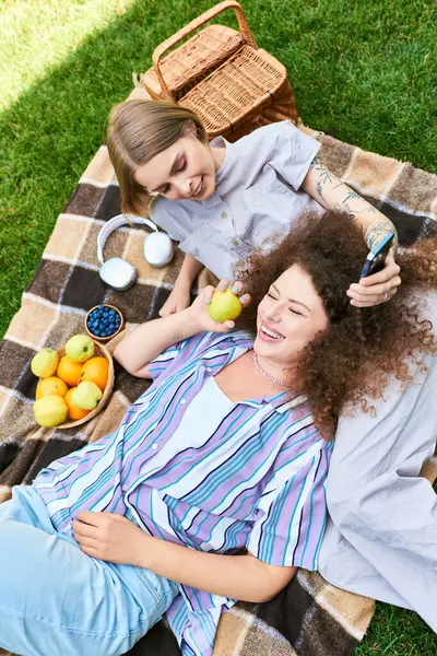 Two friends share joy while lounging on a blanket, surrounded by fresh fruits and delightful vibes. — Stock Photo