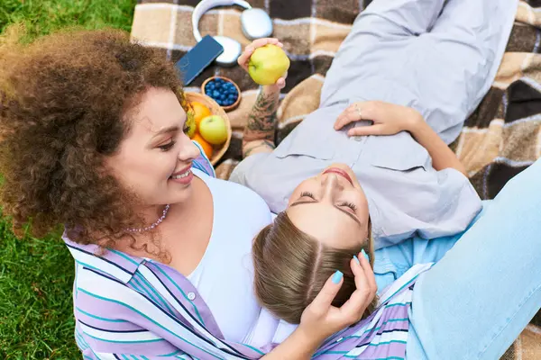 Dois amigos relaxam em um cobertor, compartilhando bons momentos com frutas e sorrisos sob o sol. — Fotografia de Stock