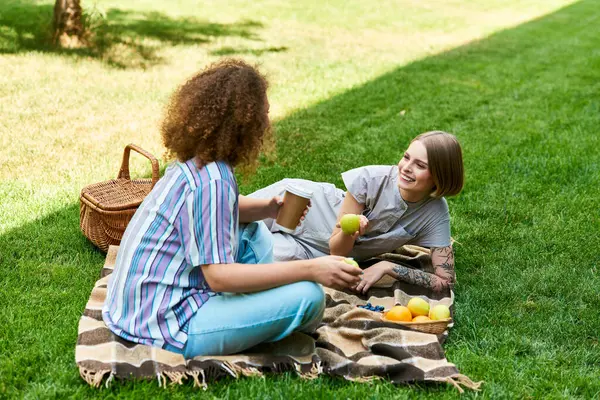 Two friends relax on a blanket, sharing fruits and joyful moments under the warm sun. — Stock Photo