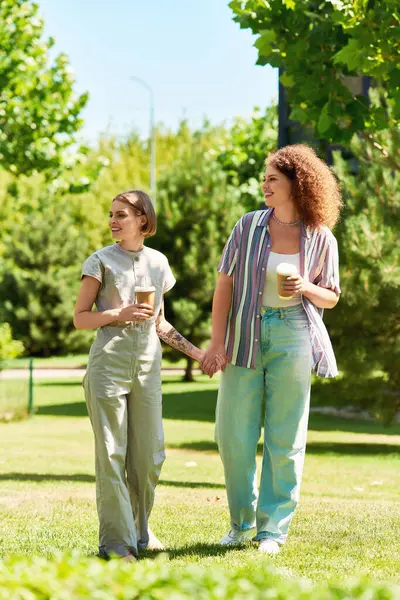 Two friends stroll through a vibrant park, sharing laughter and drinks under the sun. — Stock Photo