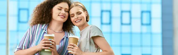 Zwei junge Frauen teilen einen Moment der Freude, nippen an Kaffee und umarmen sich in der Stadt. — Stockfoto