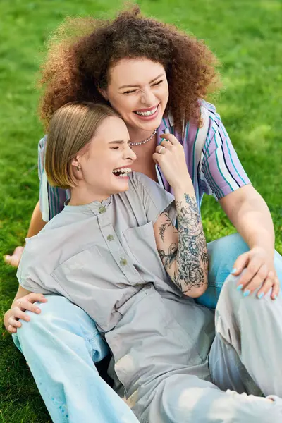 Dois amigos sentam-se na grama, compartilhando risos e abraçando um momento despreocupado juntos. — Fotografia de Stock