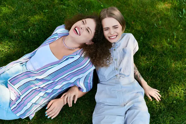 Due giovani donne si godono reciprocamente compagnia, ridendo insieme mentre giacciono sull'erba verde. — Foto stock