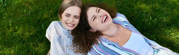Two friends enjoy a carefree moment together, laughing while relaxing on soft grass. — Stock Photo