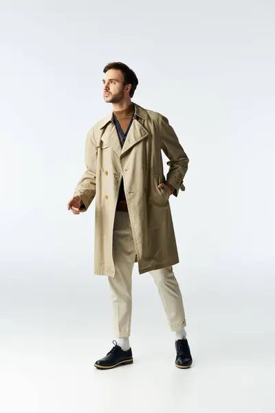 A handsome man dressed in a trendy trench coat strikes a stylish pose with poise and charisma. — Stock Photo