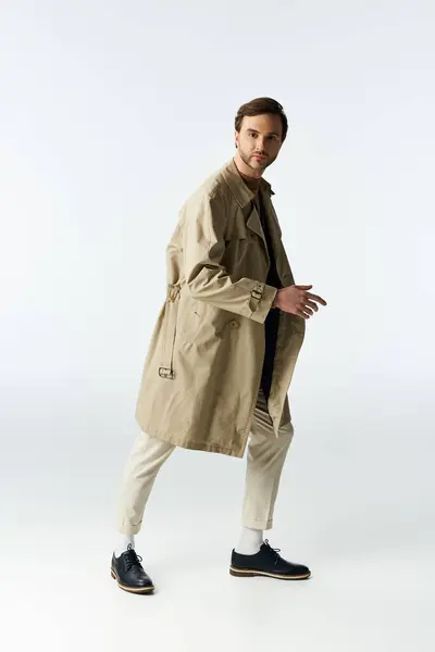 A handsome dandy clad in a light trench coat walks confidently across a minimalistic space. — Stock Photo
