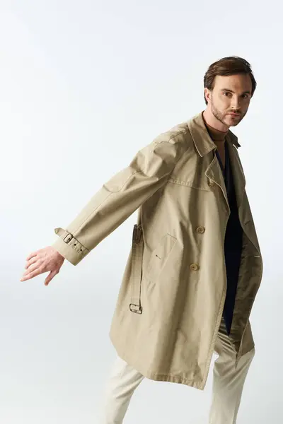 A handsome man showcasing effortless style in a light trench coat, striking a confident pose. — Stock Photo