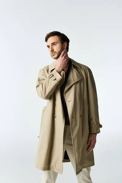 A stylish man dressed in a trench coat stands confidently, exuding elegance and charm. — Stock Photo