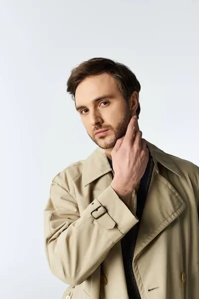 A handsome dandy adjusts his collar, exuding confidence in a sleek trench coat. — Stock Photo