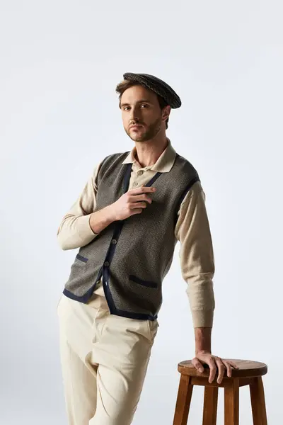 A handsome man in a stylish outfit leans confidently against a wooden stool, exuding charm. — Stock Photo