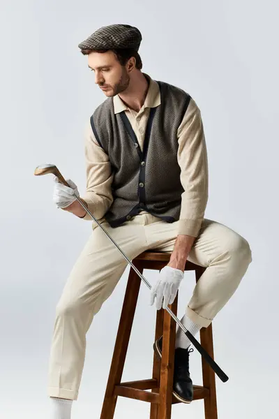 A handsome gentleman dressed in classic golf apparel contemplates his stylish equipment indoors. — Stock Photo