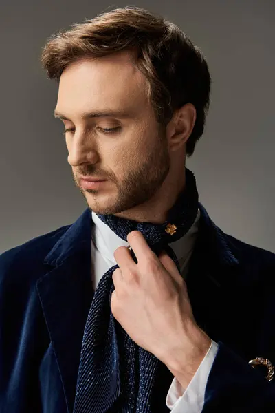 A dapper man carefully arranges his scarf while showcasing refined style in a subdued light. — Stock Photo