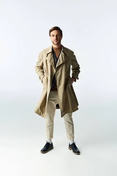 Dapper individual showcases a chic look with a trench coat and stylish shoes in a clean space. — Stock Photo