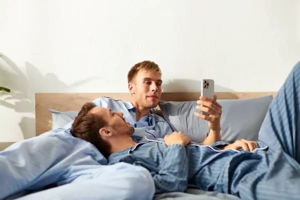 Two men enjoy a warm morning together in their pajamas while sharing a relaxed moment on their bed. — Stock Photo