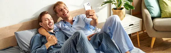 A happy gay couple in pajamas enjoys a joyful morning together, laughing and capturing the moment on their phone. — Stock Photo