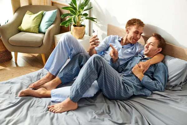 Un couple gay profite d'une matinée relaxante ensemble, partageant rires et affection tout habillé en pyjama confortable. — Photo de stock