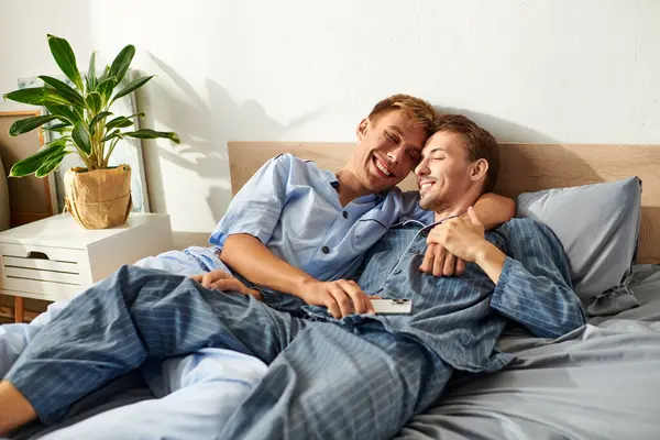 A joyful gay couple relaxes in their pajamas, embracing and enjoying a peaceful morning together. — Stock Photo