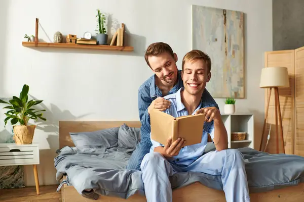 Um alegre casal gay compartilha um delicioso momento da manhã em pijama, lendo e abraçando na cama. — Fotografia de Stock