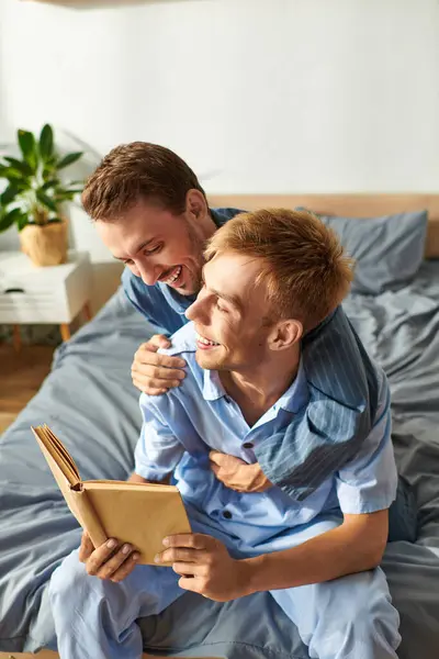 Dans la lumière du matin, un couple gay profite de l'autre compagnie, partageant des rires tout en lisant ensemble en pyjama. — Photo de stock