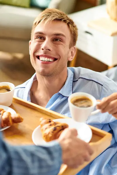A loving couple enjoys a cozy morning together, sipping coffee and sharing croissants in pajamas. — Stock Photo