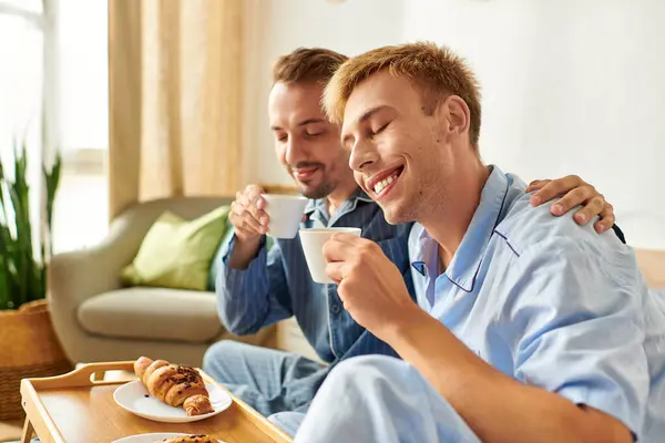 A gay couple enjoys a warm morning together in their pajamas, sipping coffee and sharing baked treats. — Stock Photo