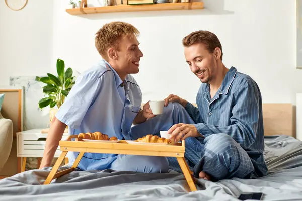 A loving couple cherishes their morning routine with coffee and pastries while cuddling in their pajamas. — Stock Photo