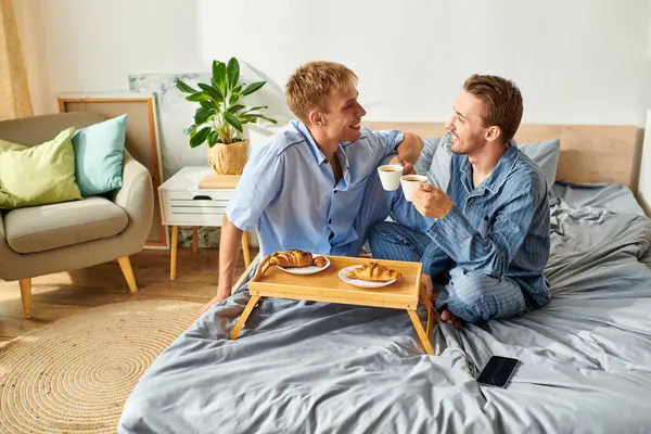 Un amorevole coppia gay gode la prima colazione in pigiama, assaporando ogni momento nel loro accogliente spazio mattutino. — Foto stock