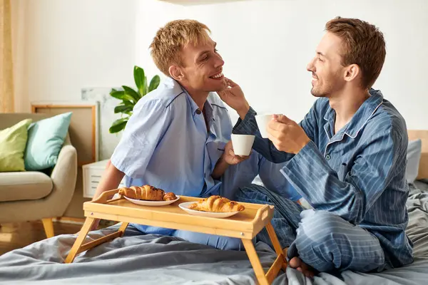 A loving gay couple enjoys a delightful breakfast together while lounging in their pajamas in the morning light. — Stock Photo