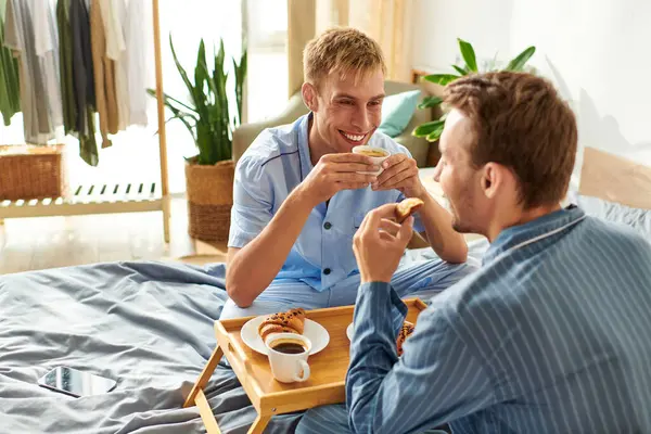 A happy couple shares breakfast in bed, savoring their time together and celebrating their love in pajamas. — Stock Photo