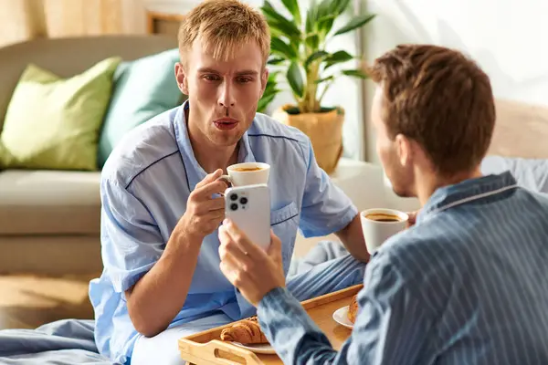A loving gay couple relaxes together in their pajamas, sipping coffee — Stock Photo