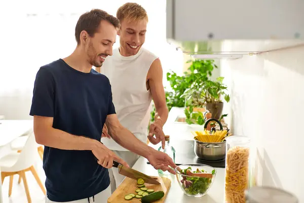 Two men happily chop vegetables and create a vibrant salad in their stylish kitchen, celebrating love. — Stock Photo