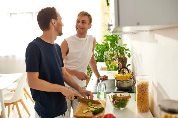 Dois parceiros amorosos sorriem enquanto cortam legumes em uma cozinha brilhante e elegante repleta de plantas. — Fotografia de Stock