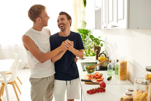 Two men share laughter and love in their modern kitchen while preparing a fresh salad together. — Stock Photo