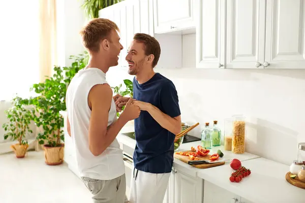 Two men happily chop vegetables and prepare a salad together in their bright, modern kitchen. — Stock Photo
