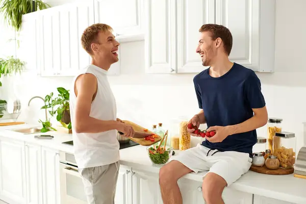A loving couple shares a joyful moment while chopping vegetables for a colorful salad in their stylish kitchen. — Stock Photo