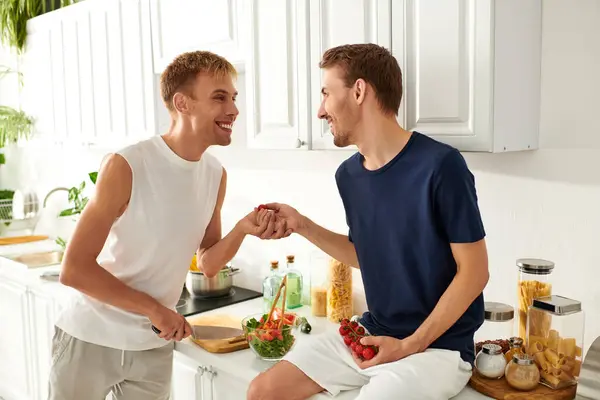 Two men joyfully chop vegetables for a salad, sharing smiles in their stylish and inviting kitchen. — Stock Photo