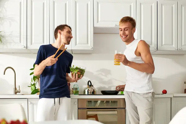 Due uomini gioiosi creano una deliziosa insalata insieme, ridono e amano riempire la loro cucina moderna.. — Foto stock