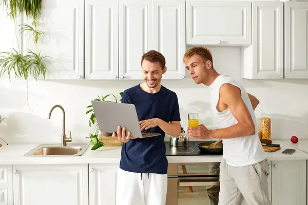 In una cucina luminosa, una coppia felice prepara un delizioso pasto guardando un computer portatile, condividendo amore e risate.. — Foto stock