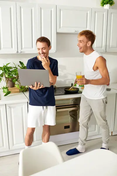 Un couple heureux faisant le déjeuner et utilisant un ordinateur portable dans leur cuisine contemporaine. — Photo de stock