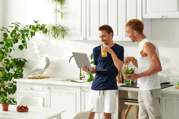 A loving gay couple enjoys cooking together and watching video in their bright kitchen. — Stock Photo
