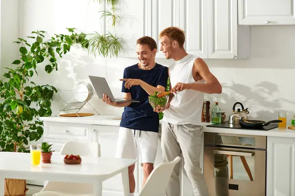 En una cocina luminosa, una pareja feliz se dedica a cocinar como ver video y disfrutar de la compañía de los demás. — Stock Photo