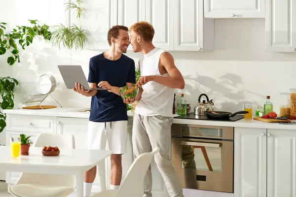 Two men are happily preparing a salad in their stylish kitchen and enjoying each others company. — Stock Photo