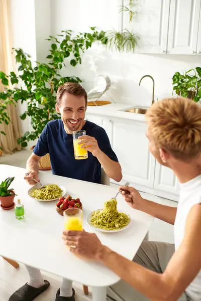 Two men eating a delicious meal together, enjoying each others company in a vibrant kitchen. — Stock Photo