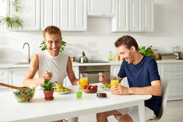 Two men share a delightful moment in a stylish kitchen while eating pasta — Stock Photo