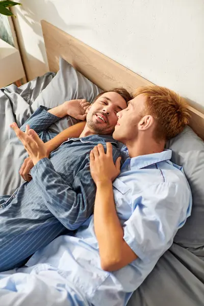 Dois homens compartilham uma manhã alegre de pijama, curtindo o riso um do outro e abraçando calorosamente na cama.. — Fotografia de Stock