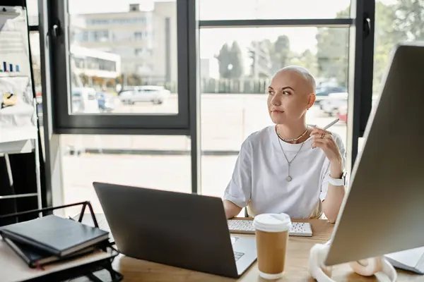 Uma jovem careca em trajes elegantes contempla enquanto trabalha em seu laptop em uma mesa. — Fotografia de Stock