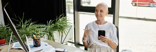 The young bald woman radiates happiness as she engages with her smartphone at a modern workspace. — Stock Photo