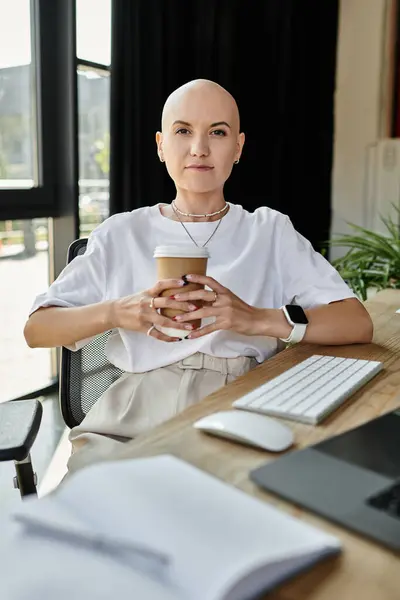 A young bald woman in stylish attire relaxes with a coffee cup at her workspace. — Photo de stock