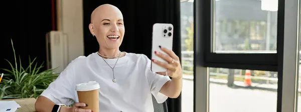 A joyful young woman in elegant attire smiles while enjoying coffee and taking a selfie. — Stock Photo
